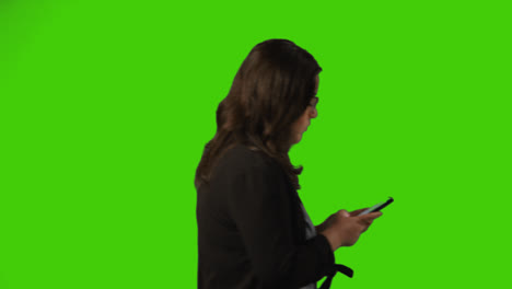 Side-View-Shot-Of-Businesswoman-Text-Messaging-On-Mobile-Phone-Walking-Across-Frame-Against-Green-Screen-1
